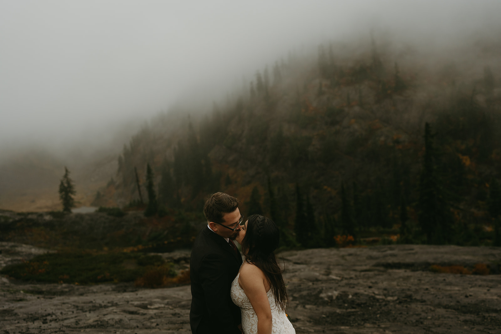 Couple sharing a kiss surrounded by fog and evergreens on their wedding day.