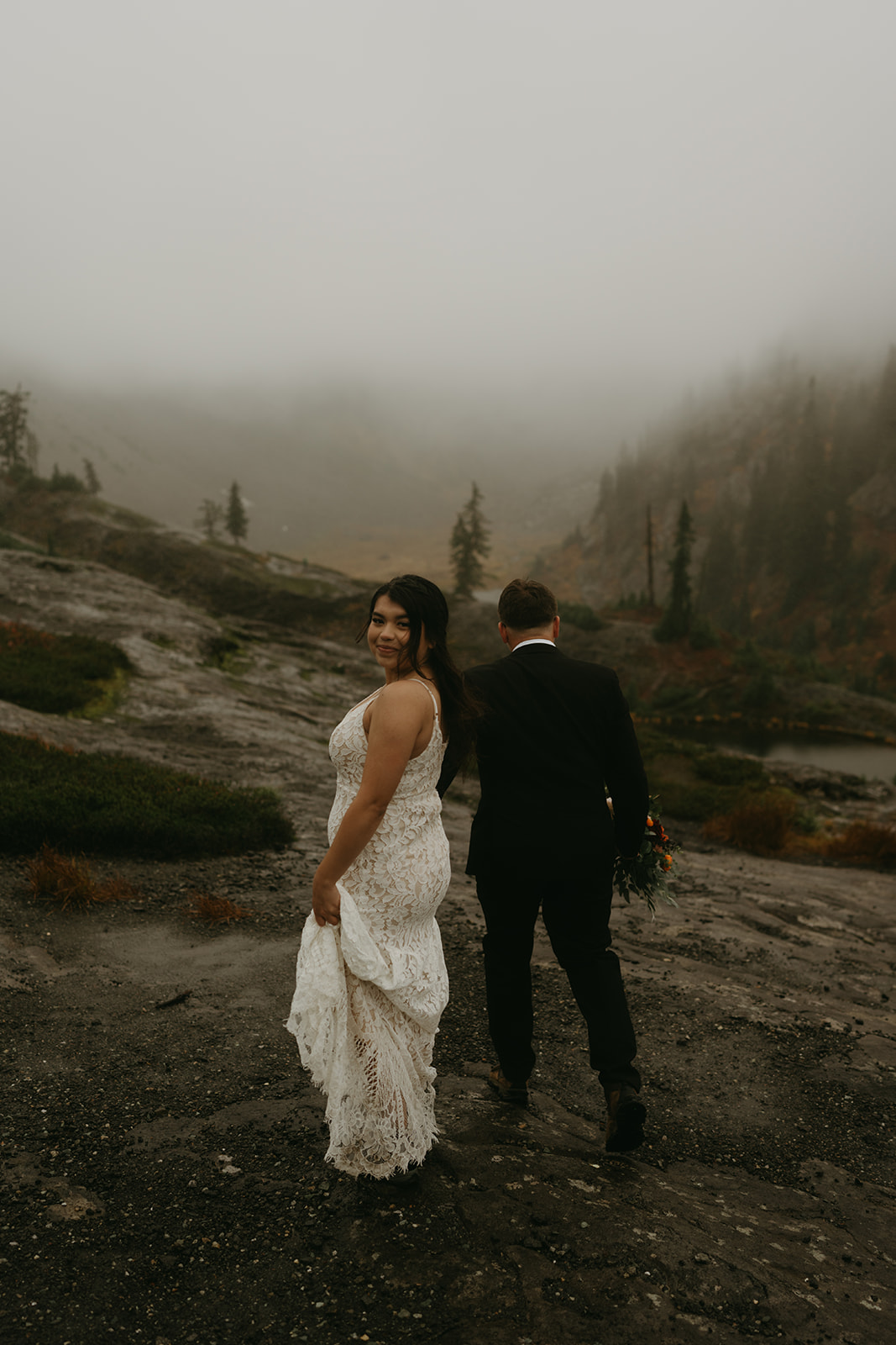 Bride looking back with a smile while walking a misty mountain trail after their elopement.