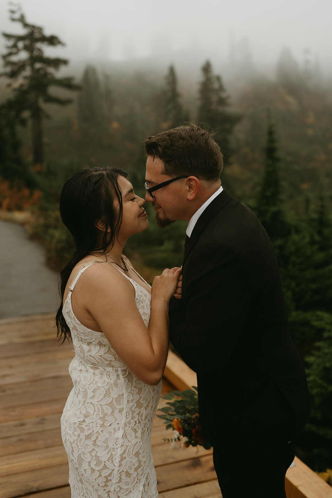Close-up of the couple leaning in with smiles, misty trees behind them during their mountain wedding.