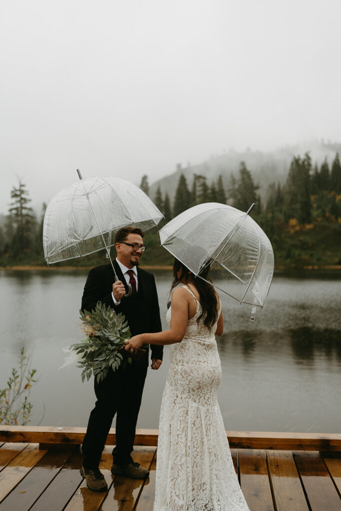 Bride and groom smiling at each other, holding umbrellas as they celebrate their mountain elopement.