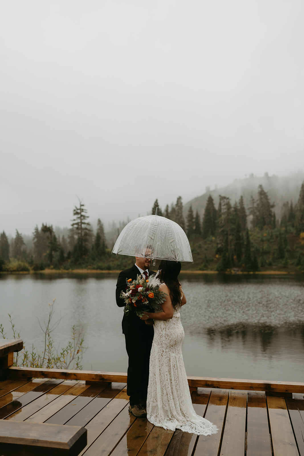Couple walking together down a wet wooden boardwalk surrounded by Washington forest.