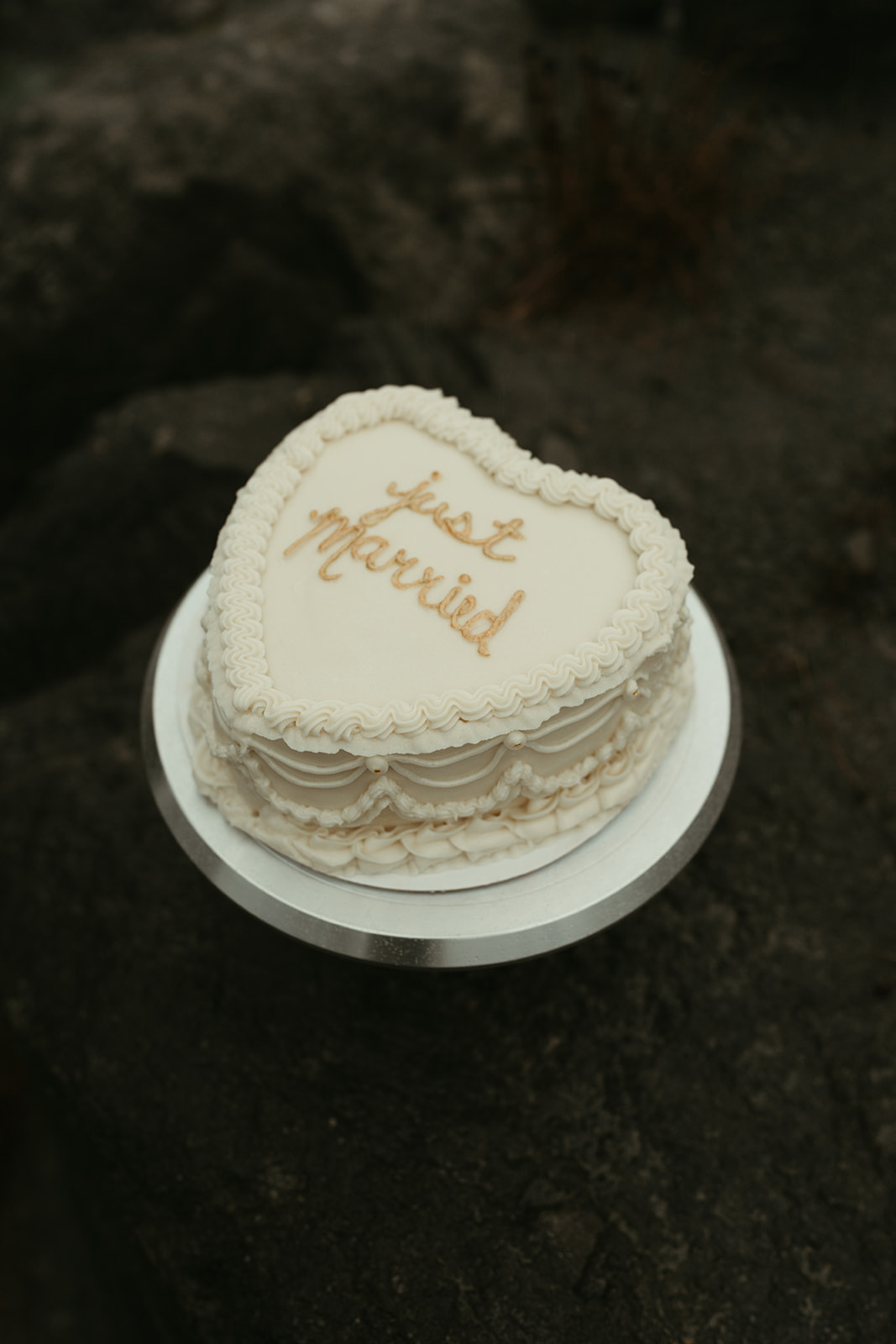 Close-up of a heart-shaped wedding cake with “just married” written in gold icing.