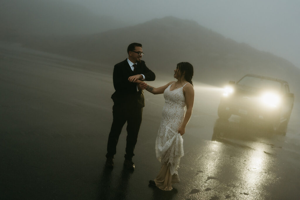 Bride and groom dancing in headlights on a foggy road during their rainy wedding.