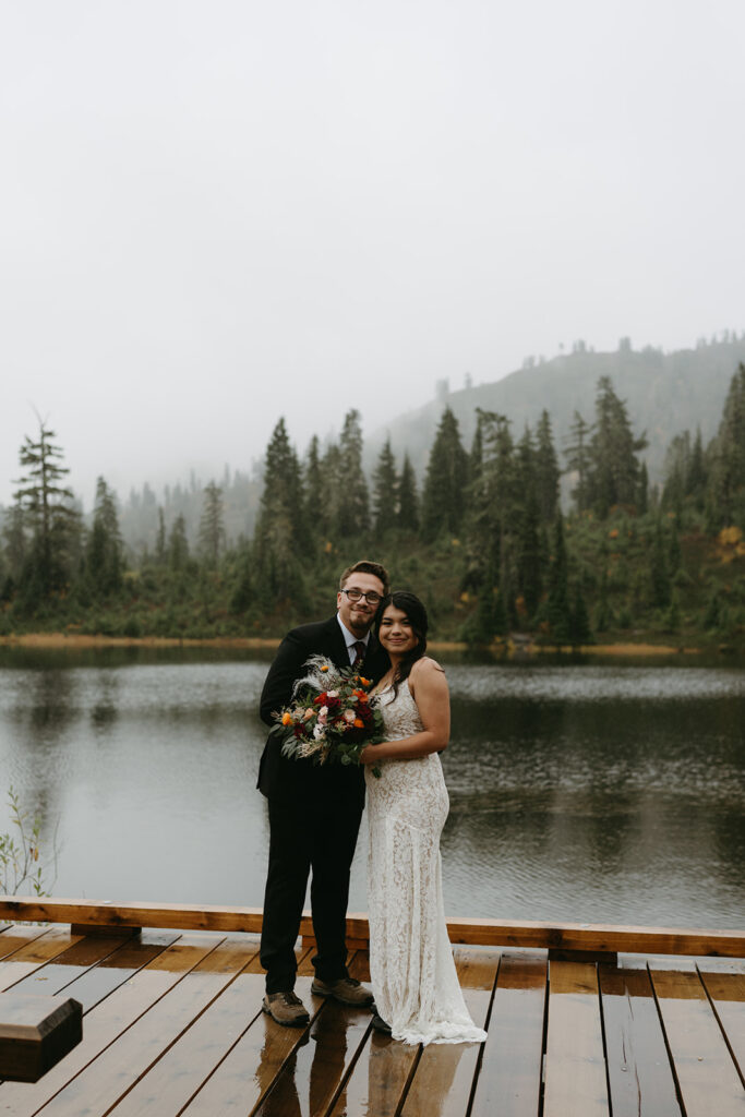 Tender embrace under a clear umbrella by the lake during a rainy wedding in the Washington mountains.