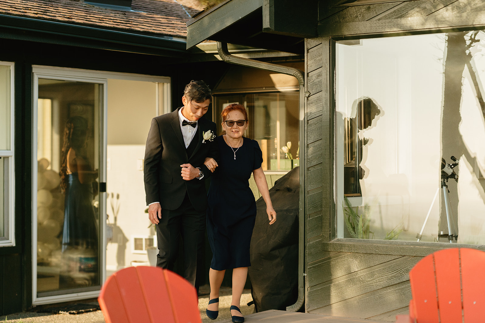 Groom walking arm in arm with his mother before the ceremony, both warmly lit by sunset.