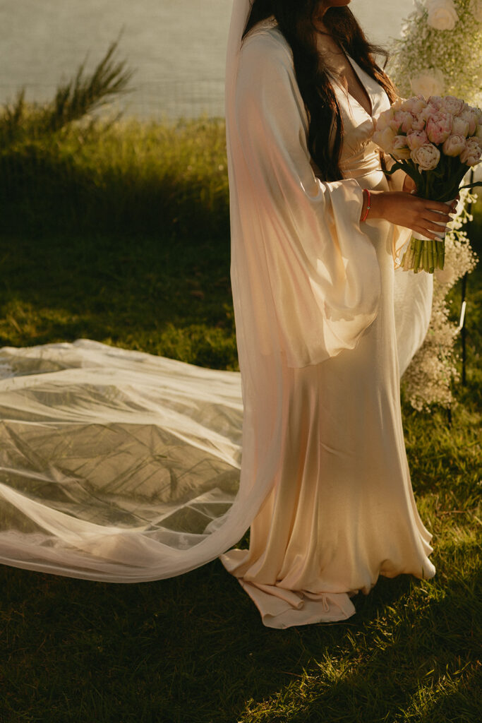Close-up of the bride holding a bouquet of tulips, her satin gown and veil trailing behind her.