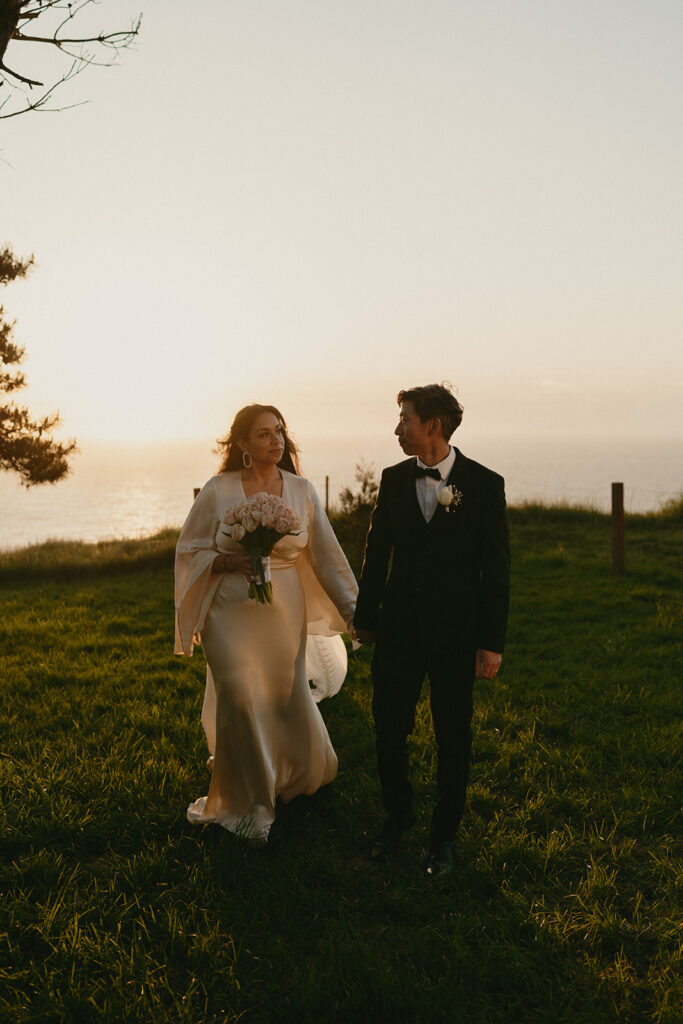 Couple walking through grass with the ocean in the background during their Whidbey Island wedding. 