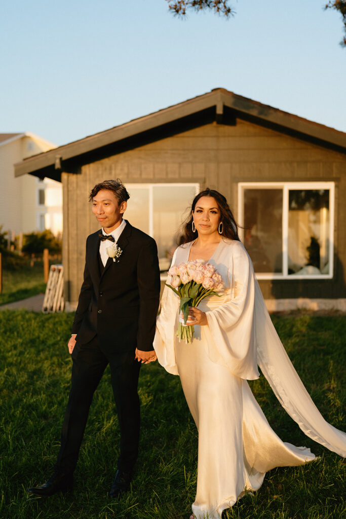 Bride and groom walking together hand in hand, warm light glowing on their elegant wedding attire.