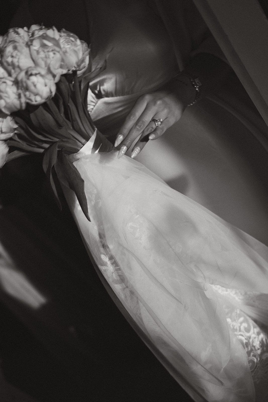 Timeless black and white photo of the bride holding her bouquet and veil, showcasing her ring.