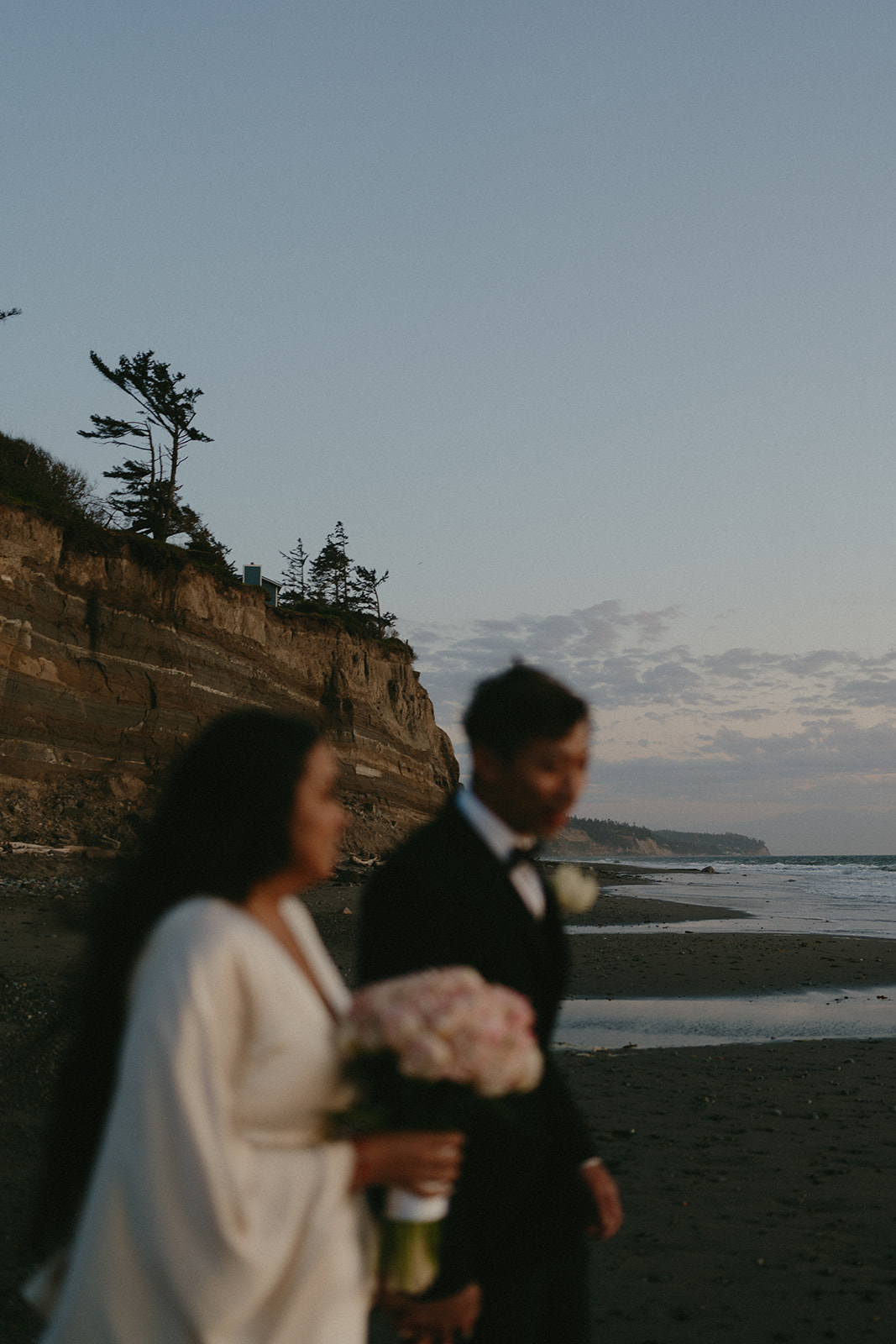 Evening stroll along the cliffs, the couple walking past driftwood and waves on Whidbey Island.