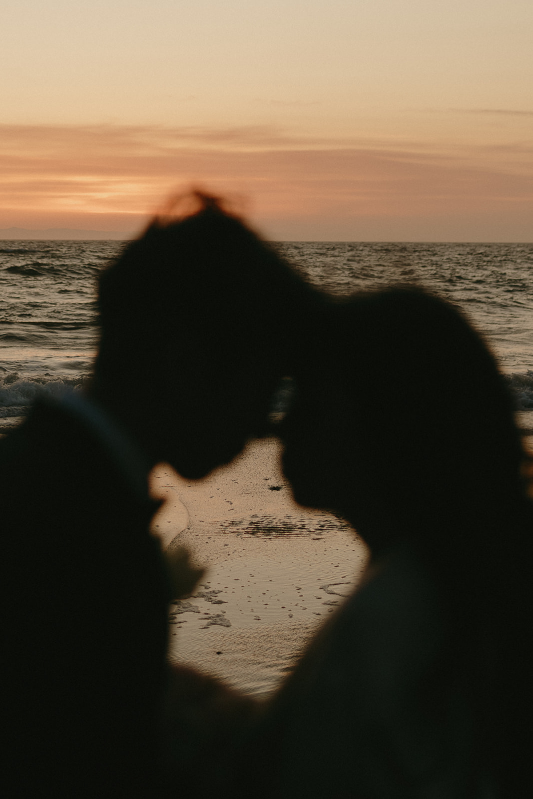 Silhouette of the couple at the edge of the sea, foreheads touching as the sun sets behind them.