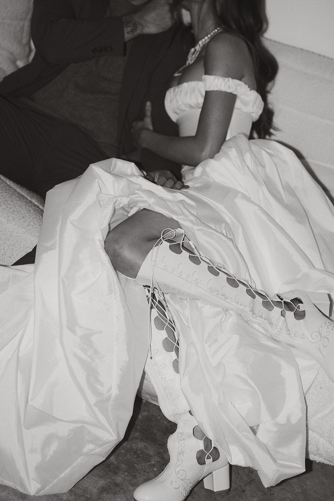 A black-and-white close-up of the bride’s embroidered boots and flowing dress as she sits close to her groom, their moment quiet and tender.
