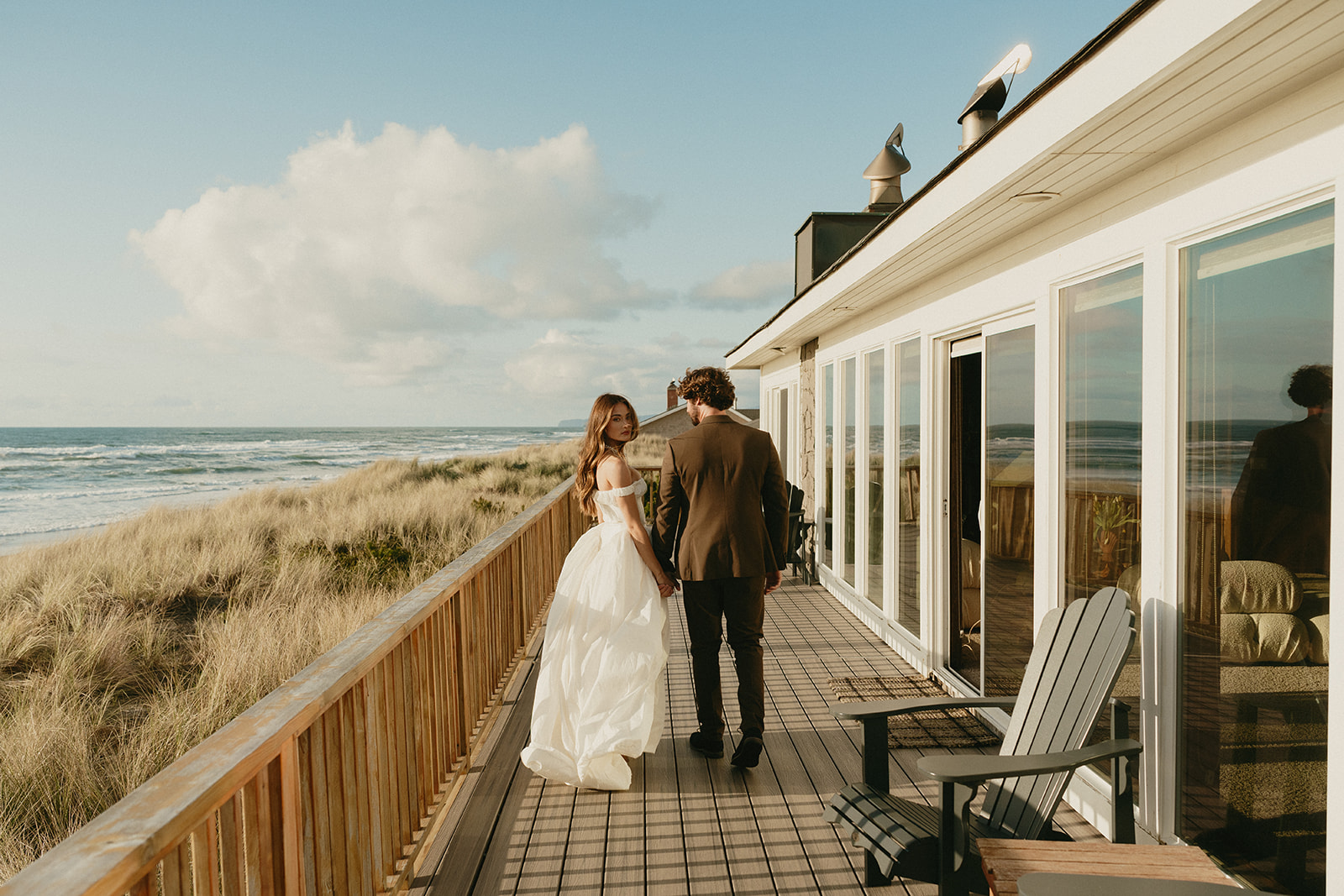 An Oregon Coast elopement morning unfolds on a quiet deck overlooking the sea, as the couple walks hand in hand beside a coastal beach house.