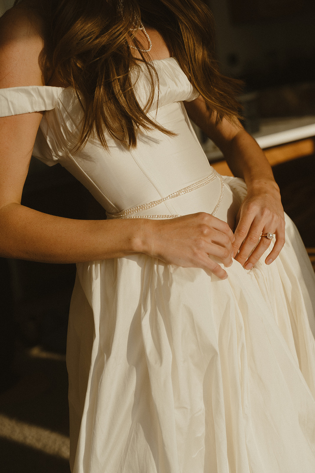 Hands gently smoothing the waist of a wedding dress, capturing the final quiet moments before the ceremony begins.