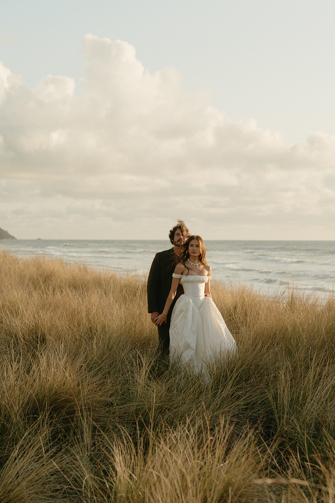 Couple standing close in golden grass with the Pacific Ocean behind them during their intimate Oregon Coast elopement.