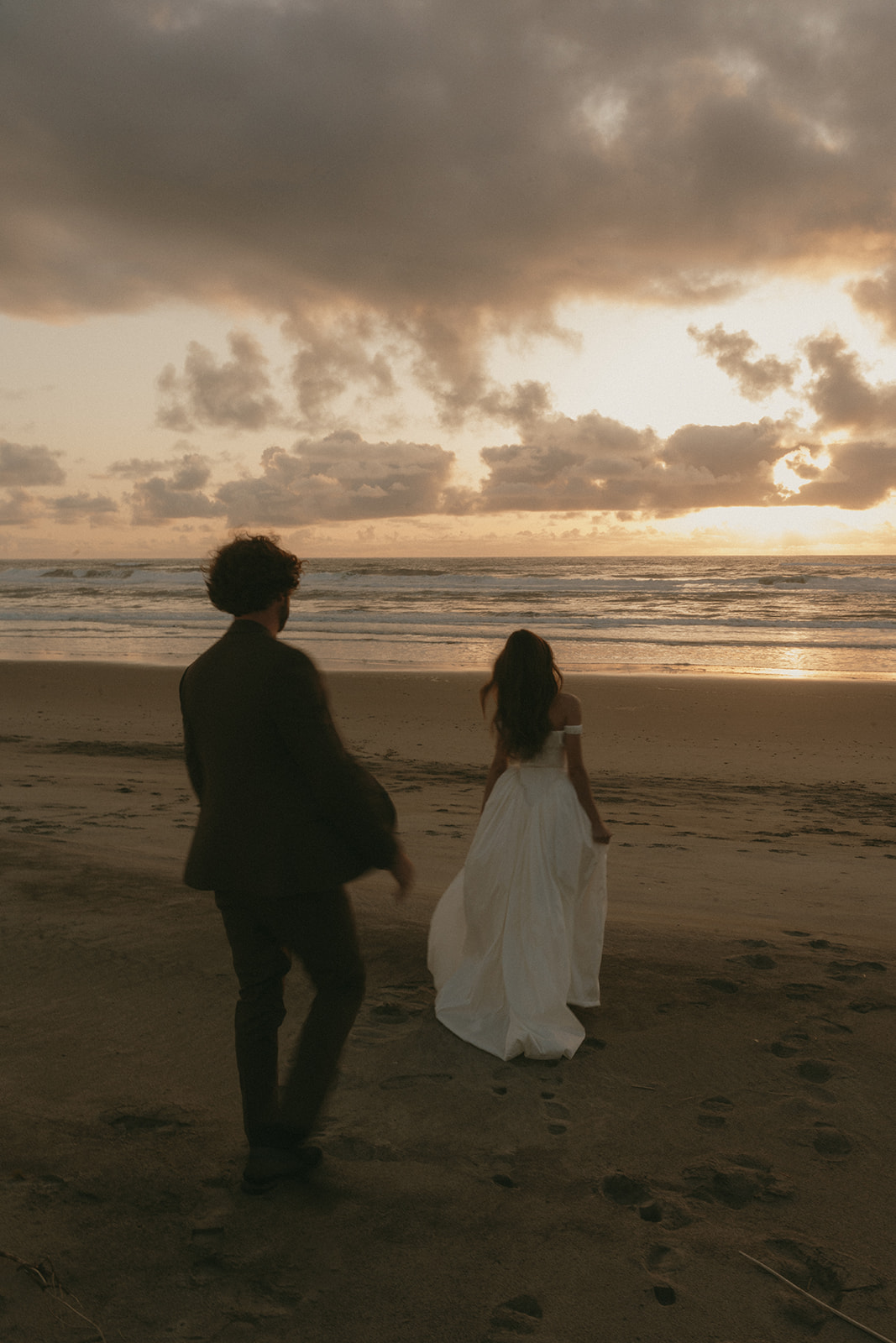 Bride and groom walking side-by-side on the beach at golden hour during their Oregon Coast elopement, leaving footprints in the sand.