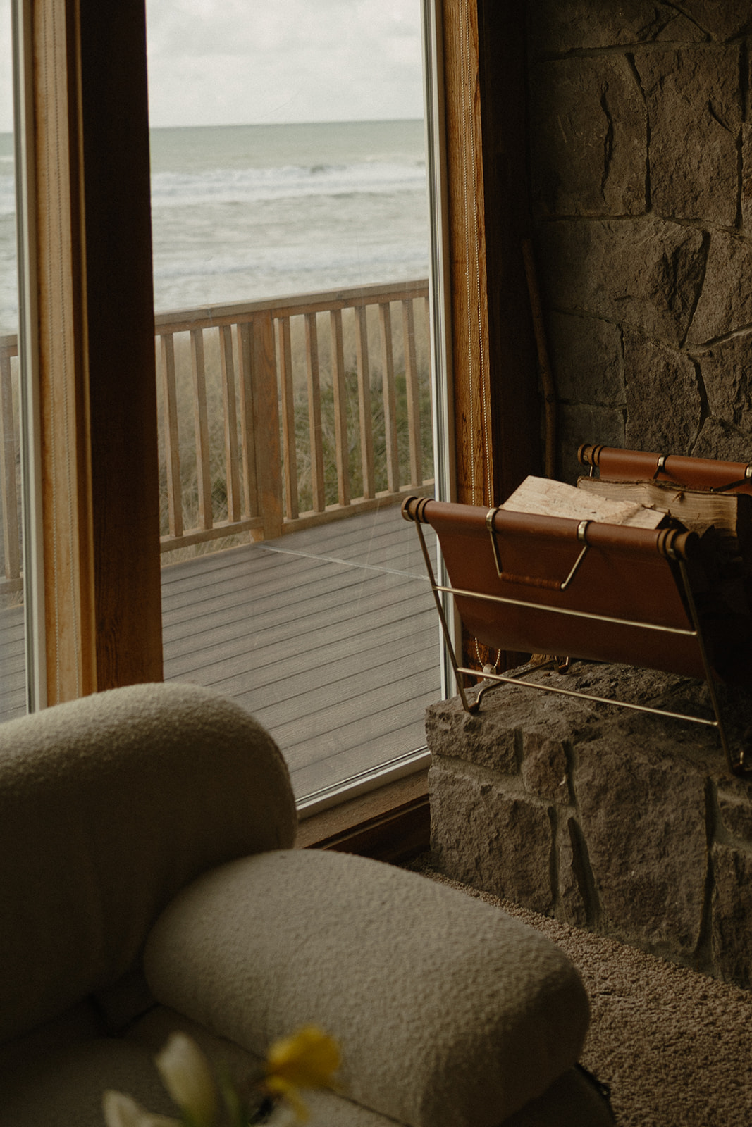Firewood rests by the stone hearth beside a window looking out over the waves, part of a warm coastal setting for this Oregon Coast elopement day.