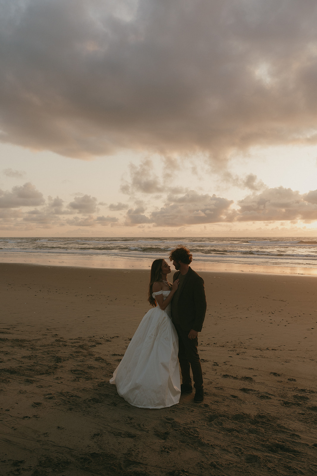 Bride laughing and holding her dress as she walks through tall beach grass toward her partner during an Oregon Coast elopement.