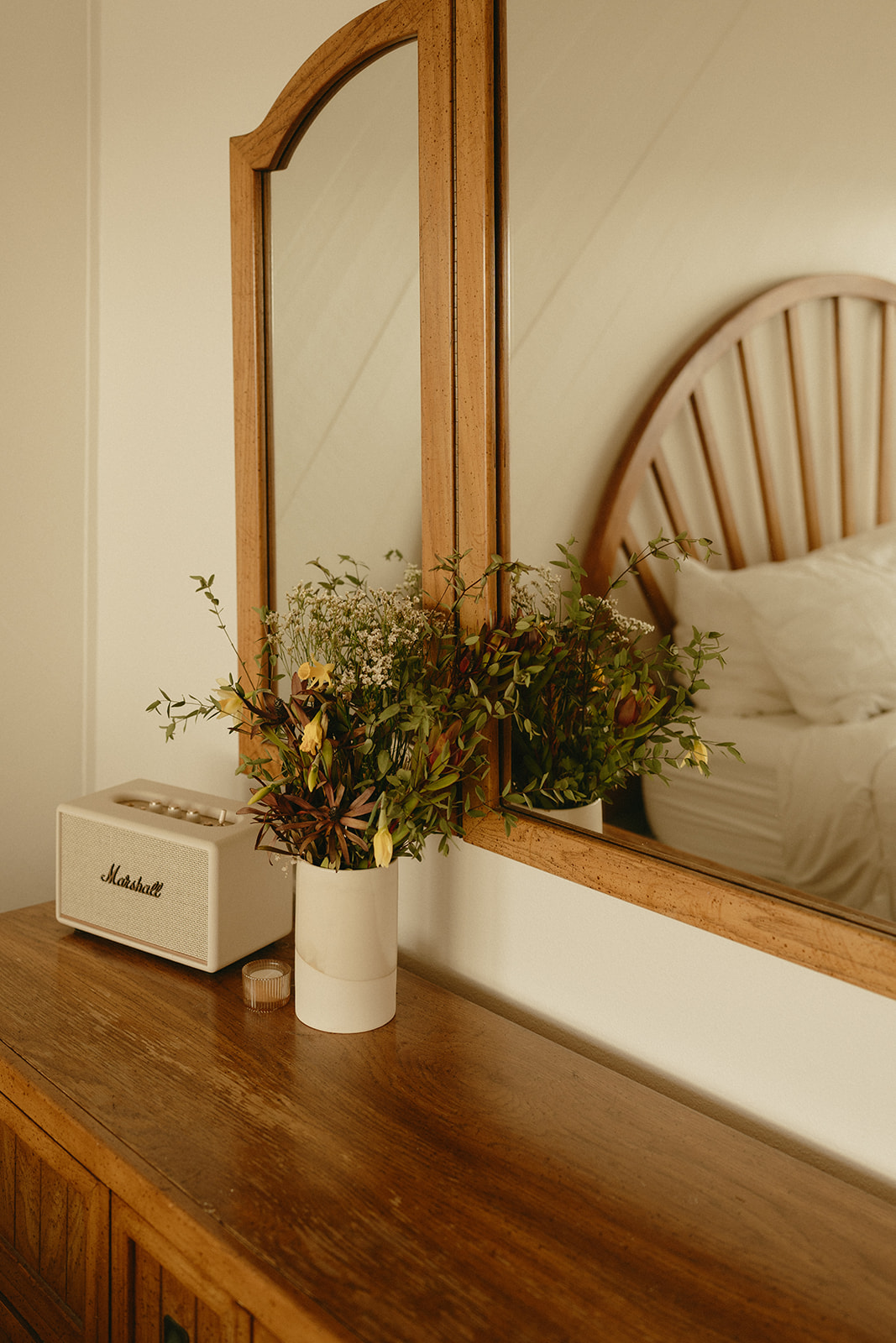 A bundle of greenery and wild florals in a ceramic vase reflects in a vintage wooden mirror, evoking a calm and grounded bridal morning.