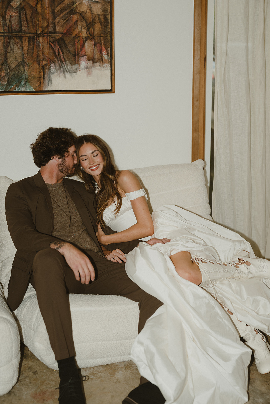 The couple curls up together on a cozy cream sofa after their Oregon Coast elopement, sharing quiet laughter and tender closeness.