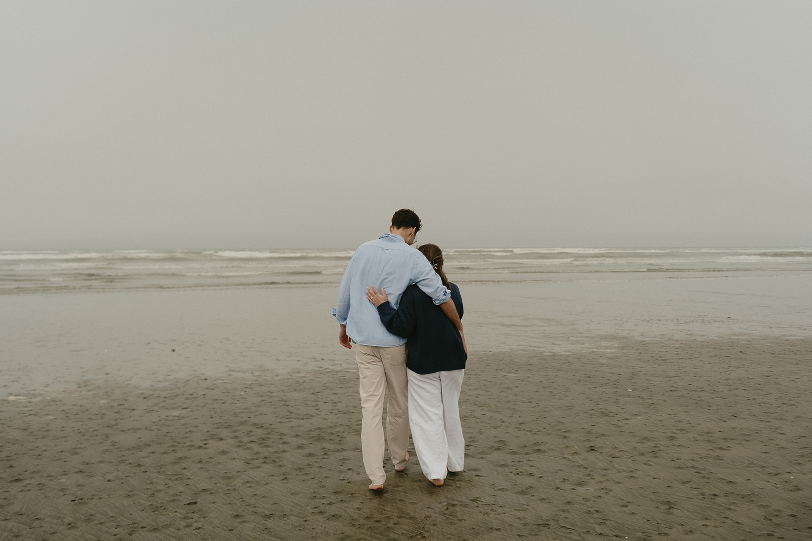 Couple walking barefoot along a misty shoreline, arm in arm, their connection quiet and strong.