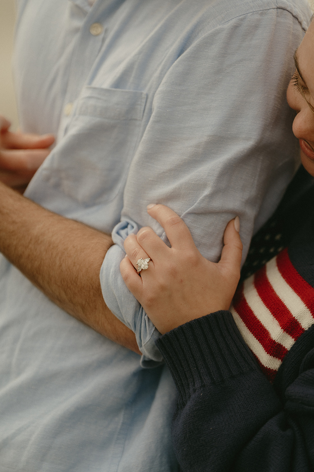 Close-up of a woman holding her partner’s arm, her engagement ring glimmering softly against his shirt.