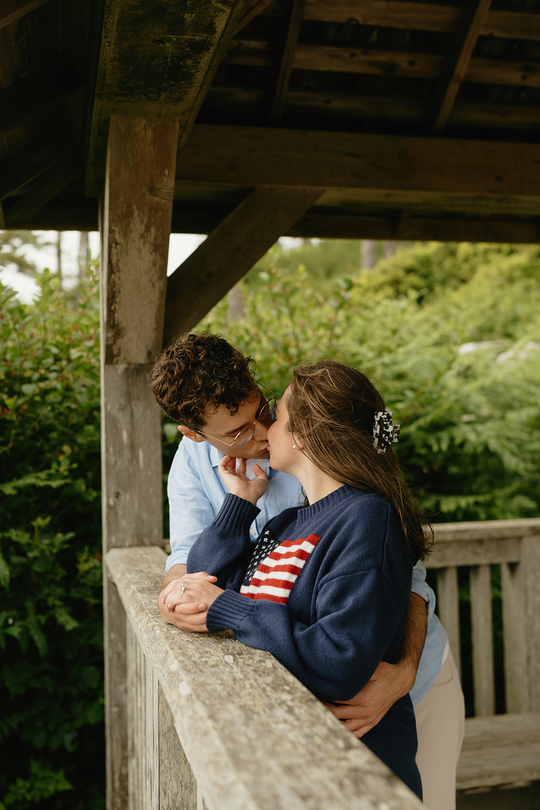 Couple leaning in for a kiss on a wooden gazebo, a romantic setting that offers timeless ideas for engagement photos.