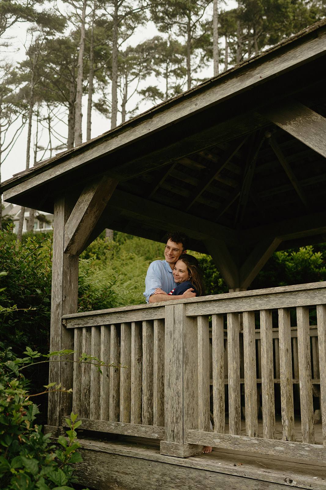 Couple wrapped in a peaceful embrace on the porch of a rustic wooden gazebo—natural, cozy ideas for engagement photos in the Pacific Northwest.