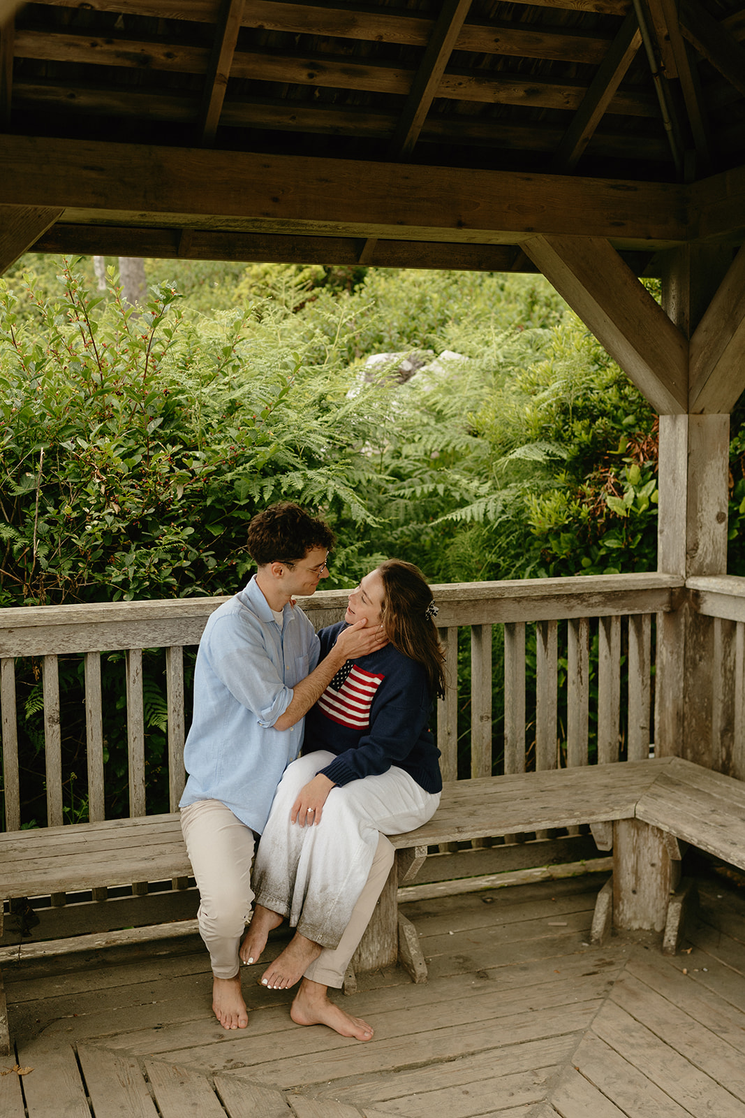 Couple sitting barefoot together in a rustic wooden gazebo, sharing an intimate moment.