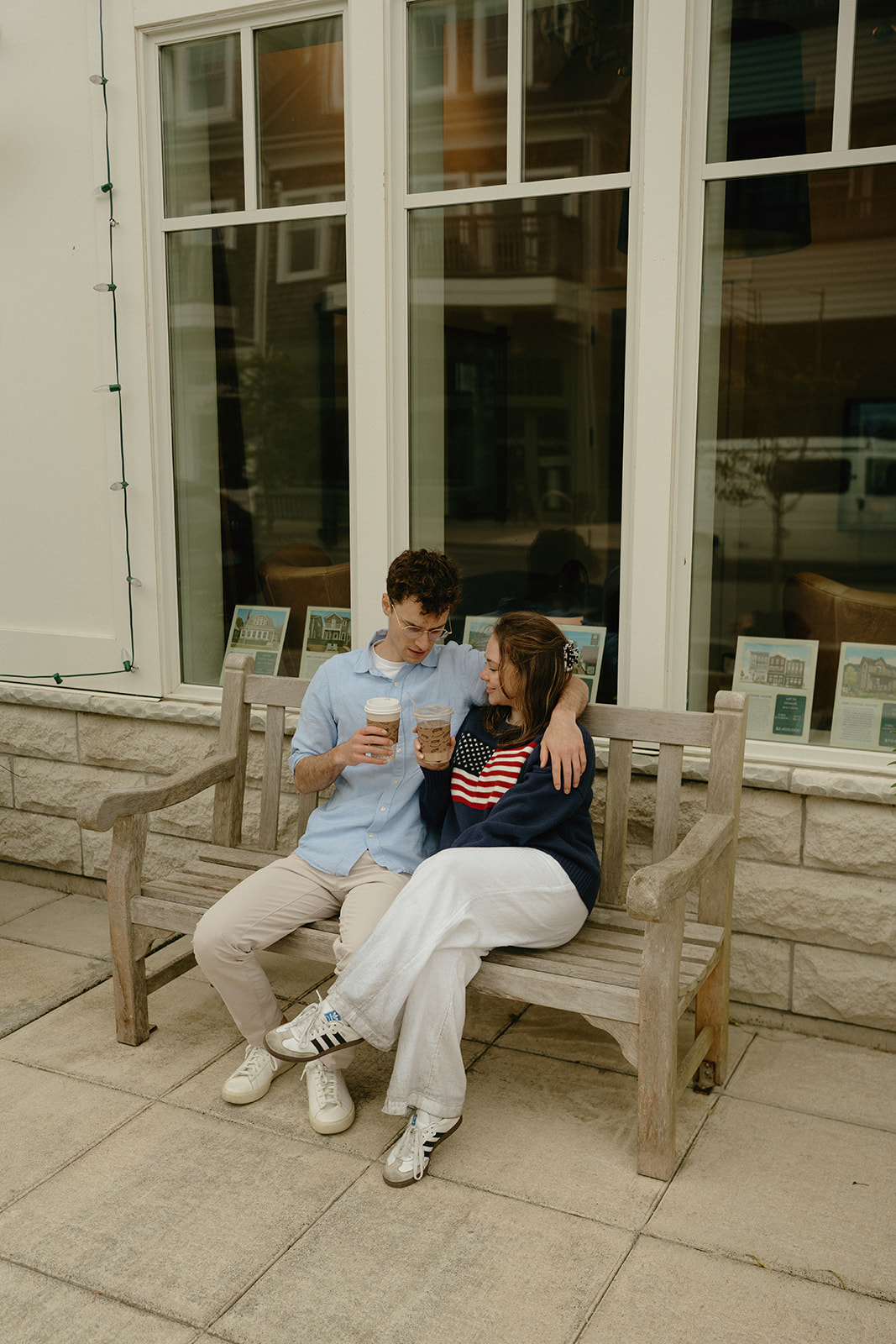 Couple sitting close on a wooden bench with coffee in hand, relaxed and happy on a calm afternoon stroll.