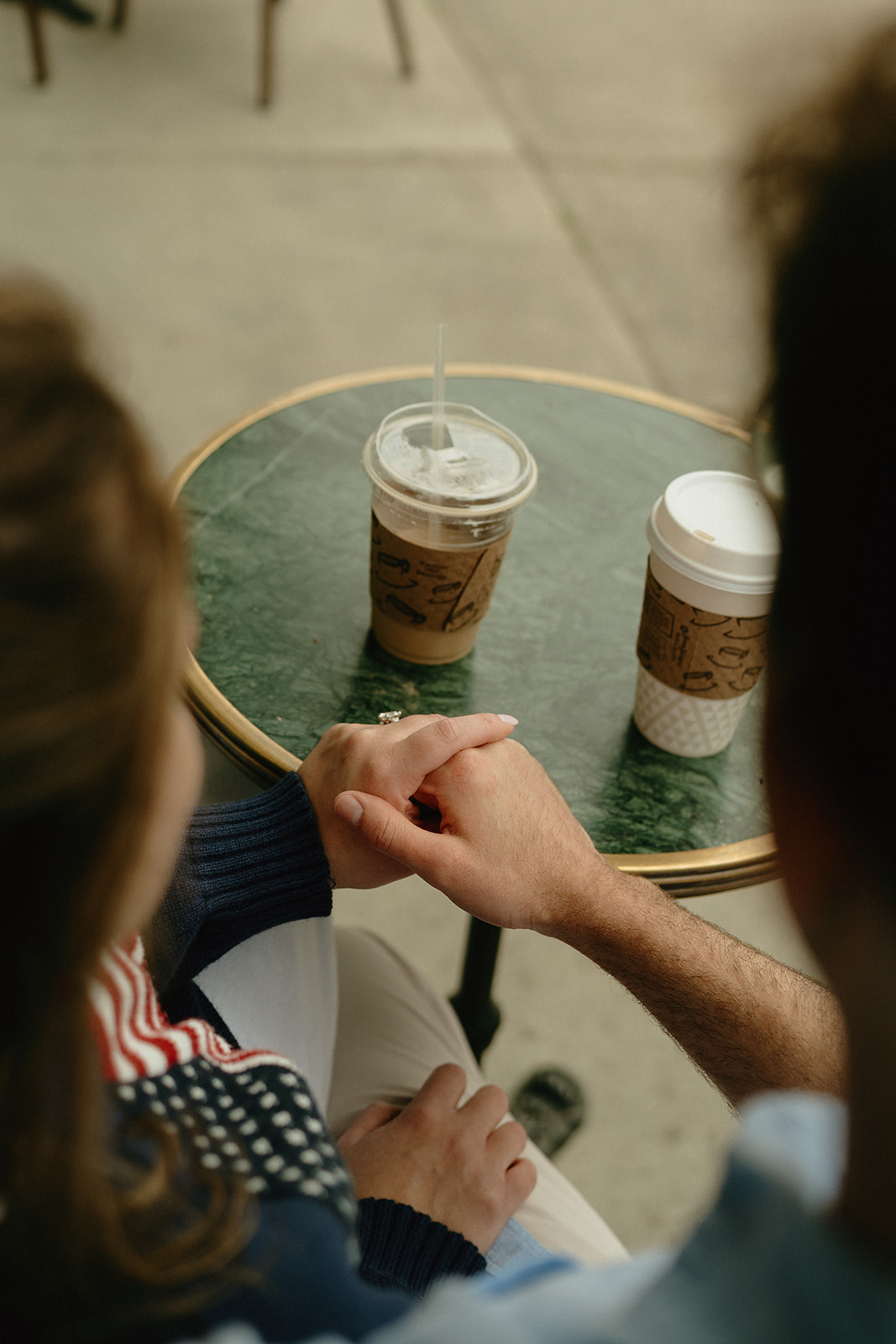 Close-up of couple holding hands over a green café table with coffee drinks, a quiet and tender gesture.
