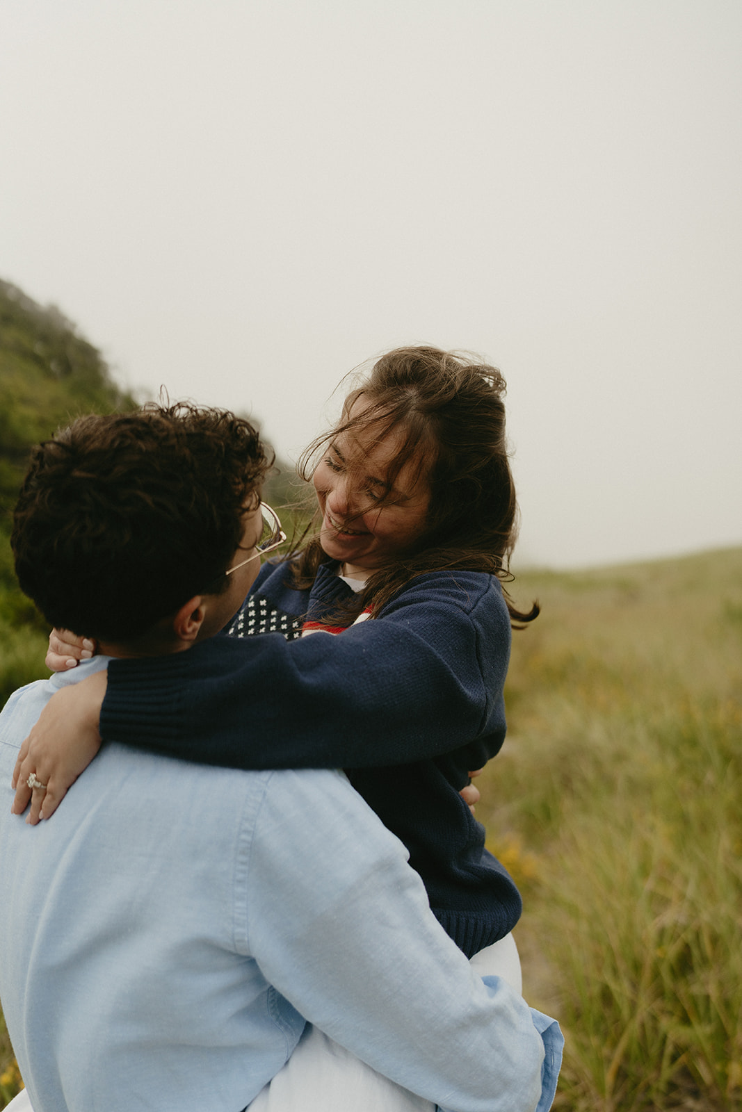 Man holding his partner in his arms in a foggy field, her smile full of joy and love—one of many natural ideas for engagement photos in the Pacific Northwest.