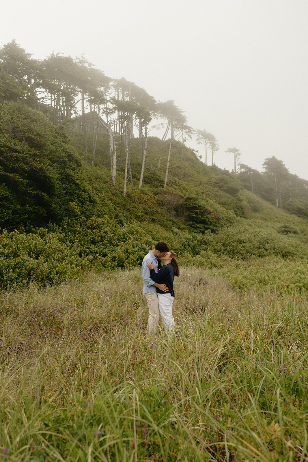 Romantic moment between a couple standing in coastal grass, wrapped in each other’s arms—ideal for couples searching for ideas for engagement photos with natural backdrops.