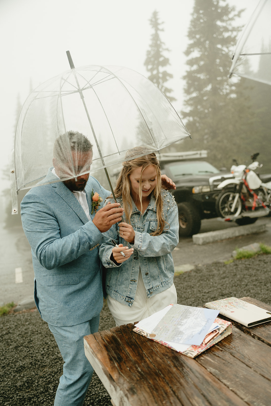 Newly married couple signing marriage license while holding clear umbrella after Mount Rainier national park elopement