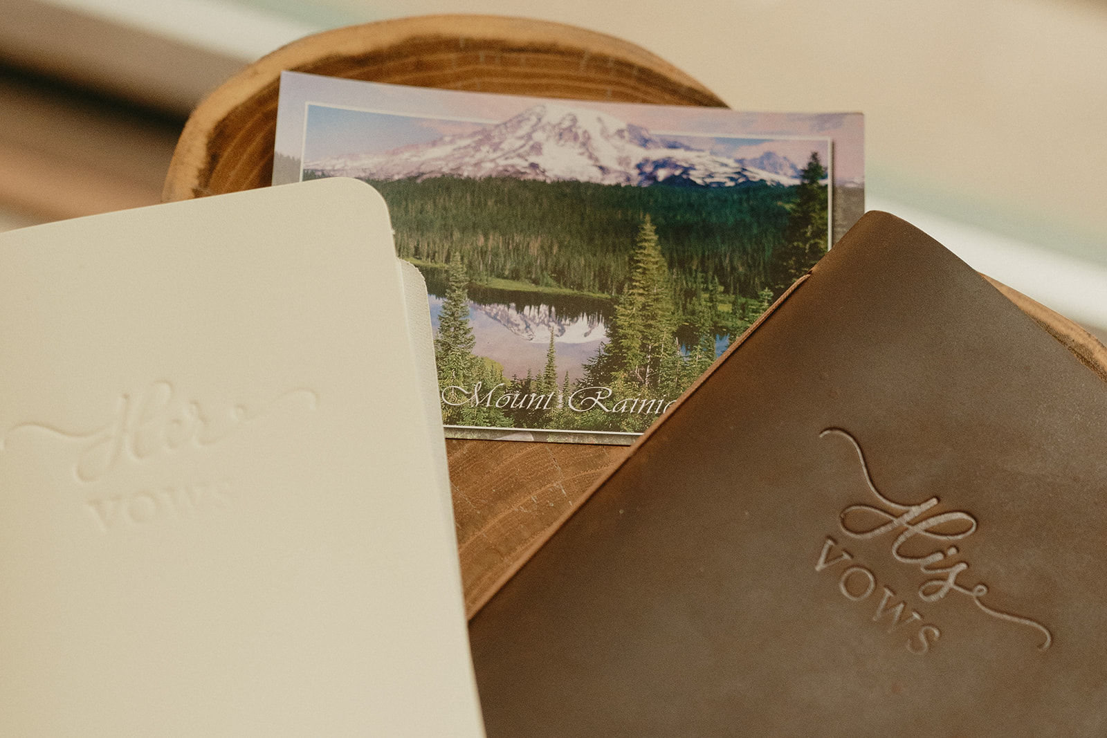 Cream and brown leather vow books sitting on top of a postcard for Mount Rainier