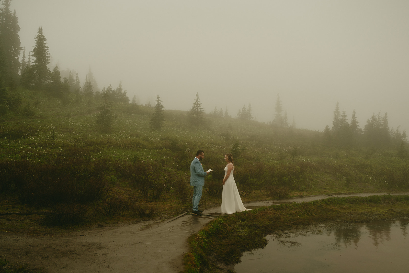 Elopement vows exchanged beside a reflective pool, surrounded by greenery and low clouds in Mount Rainier National Park.