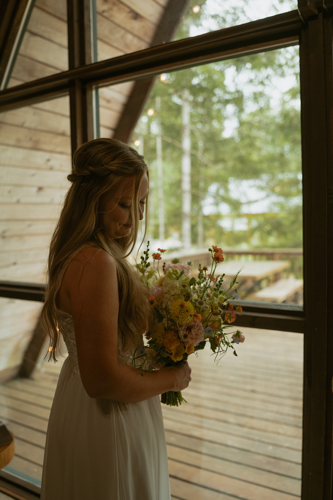 Bride holding various colored flowers in bouquet while standing in front of window