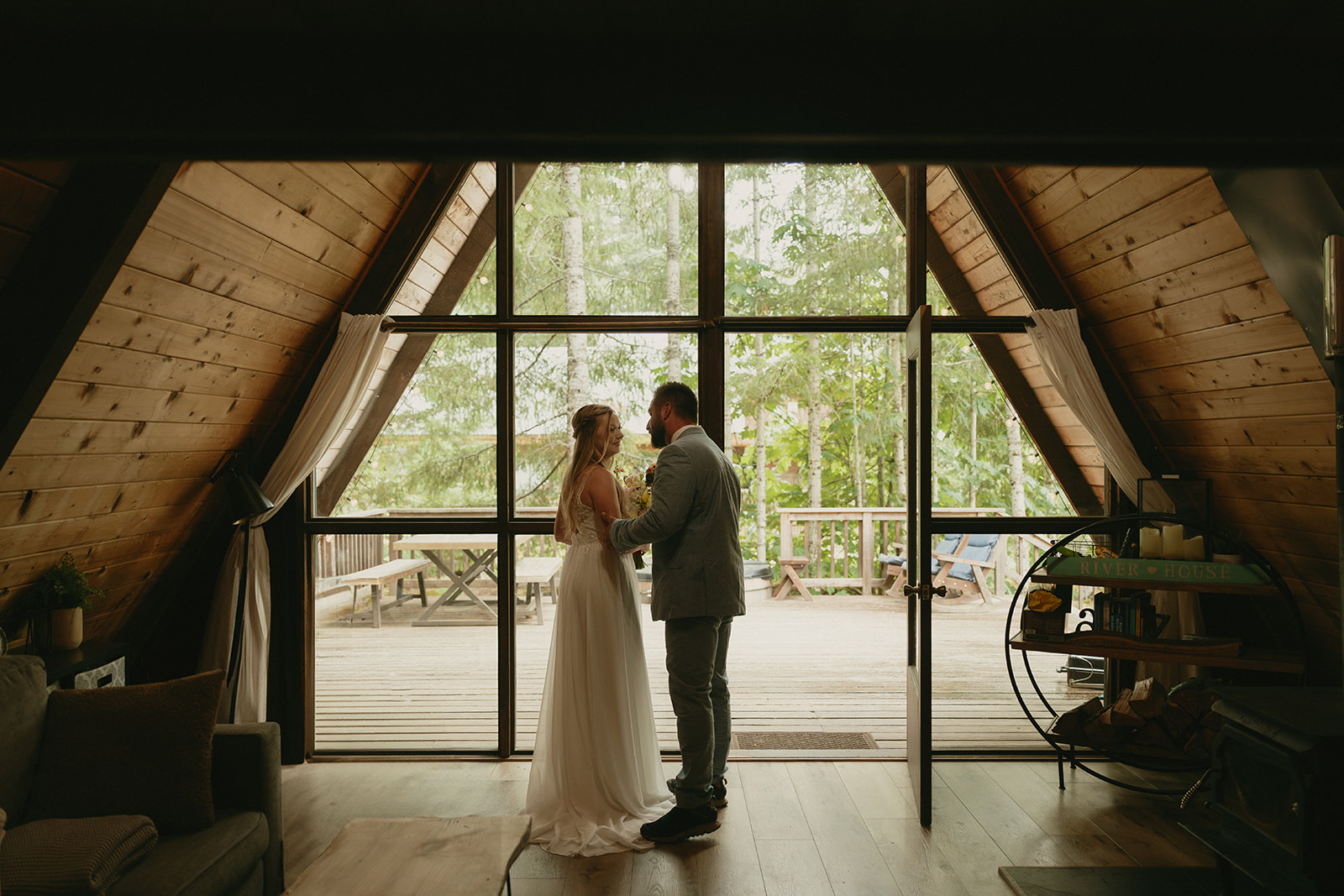 Bride and groom embracing while standing beside window with natural light coming in