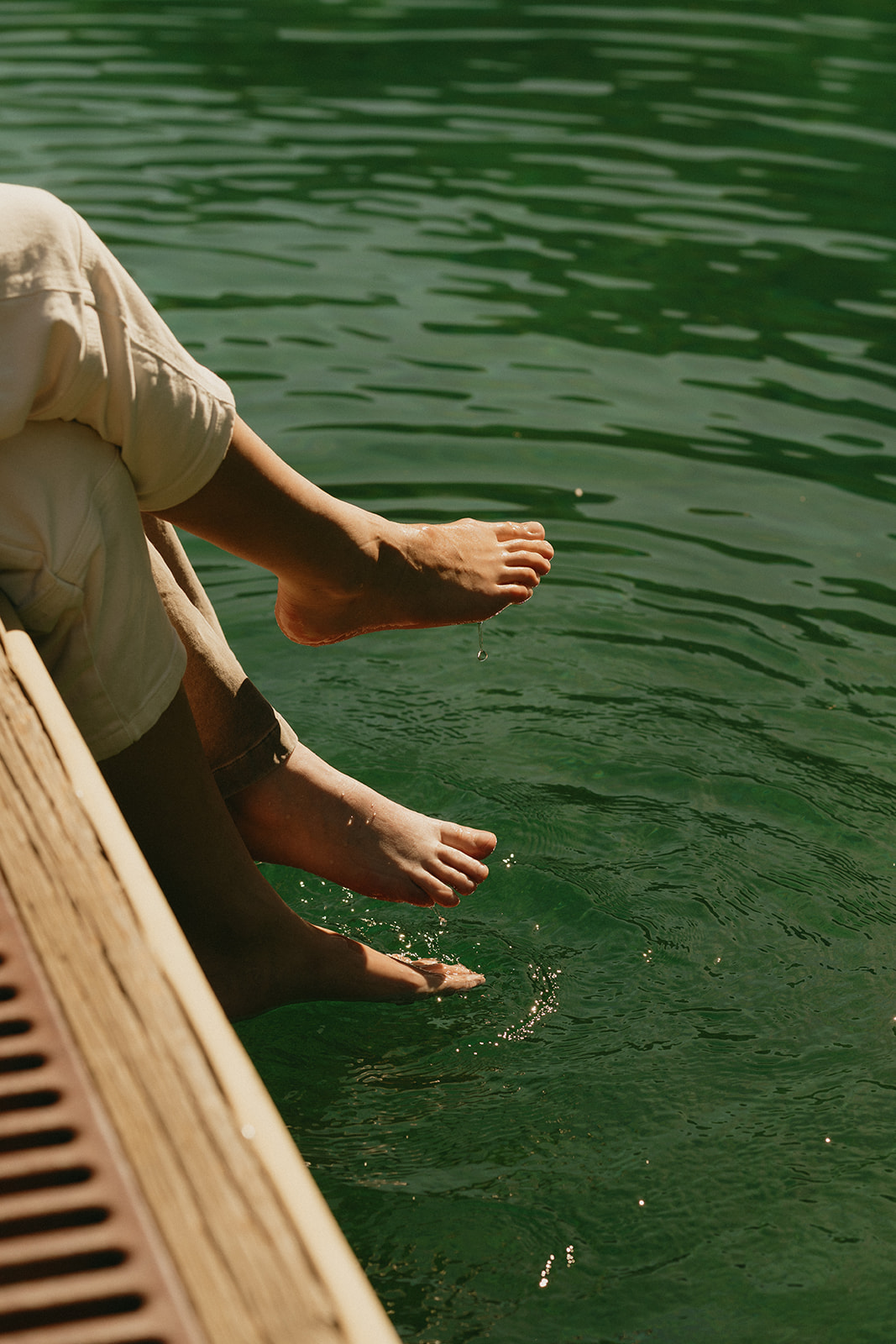 Feet dangle over the edge of a dock, skimming the water’s surface in the late afternoon sun.