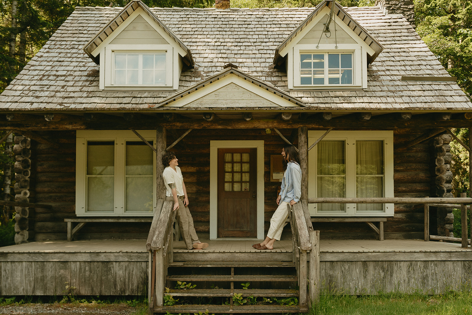 A wide shot of a couple standing on opposite sides of a charming forest cabin, their connection holding steady across the porch.