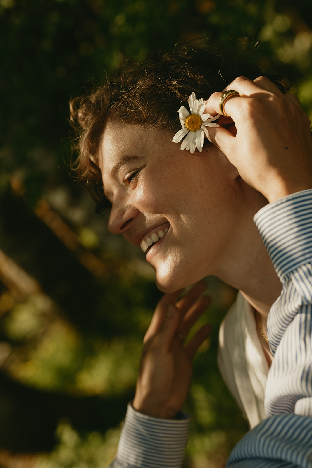 A close-up moment of one partner tucking a daisy behind the other’s ear, captured with golden sunlight and soft smiles.