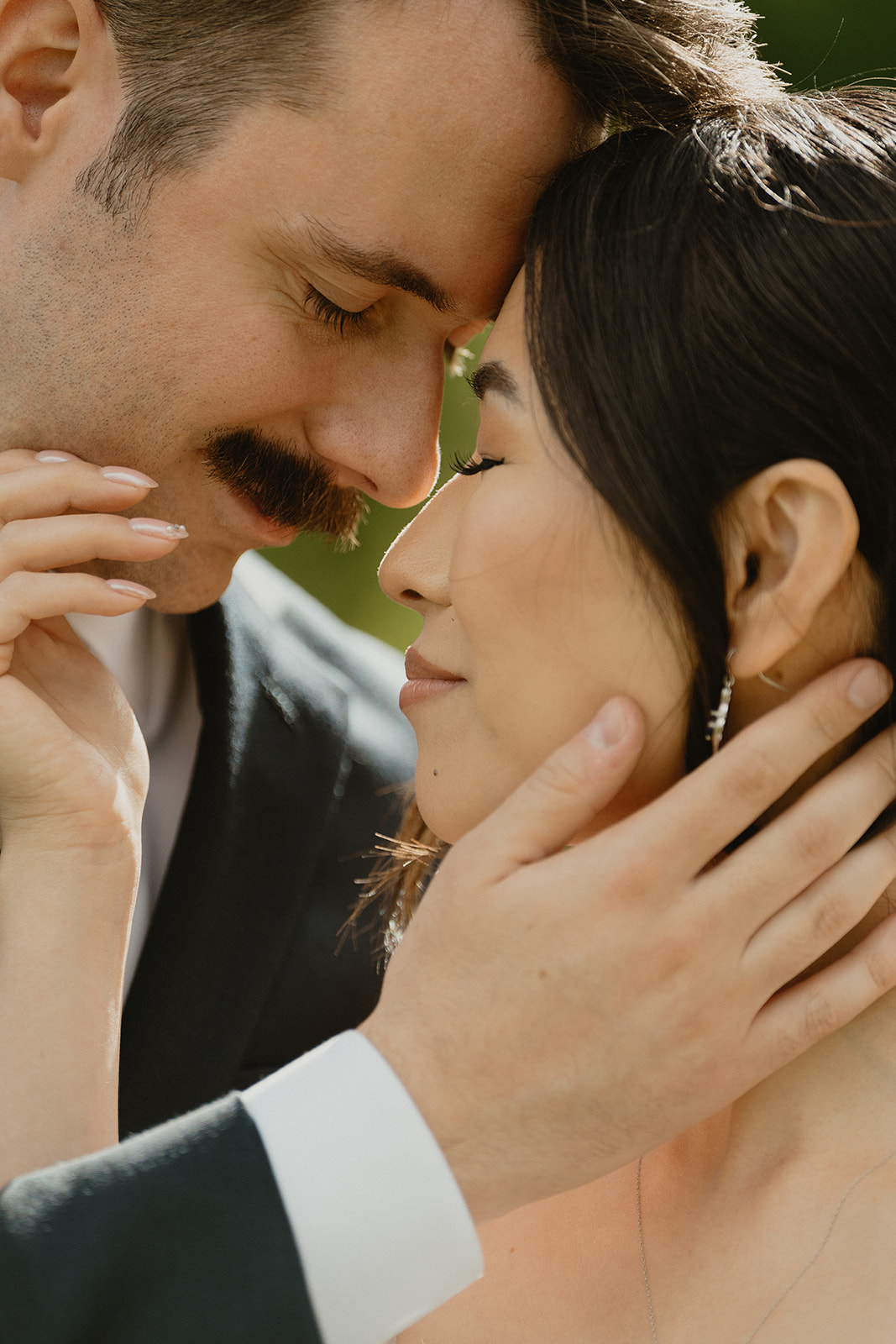 Tender close-up of a bride and groom with foreheads touching, eyes closed in quiet connection.