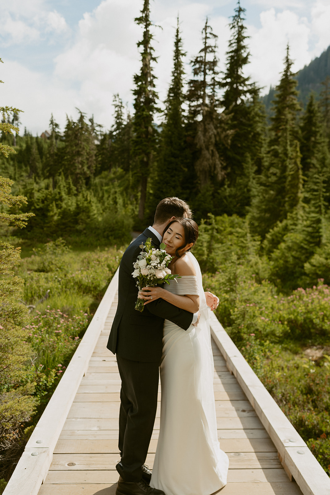 Bride and groom share a quiet hug on a wooden boardwalk in the Washington mountains.