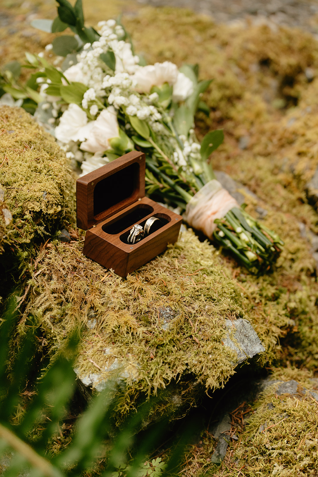 Close-up of wedding rings in a wooden box with bouquet, captured during an elopement in Washington.