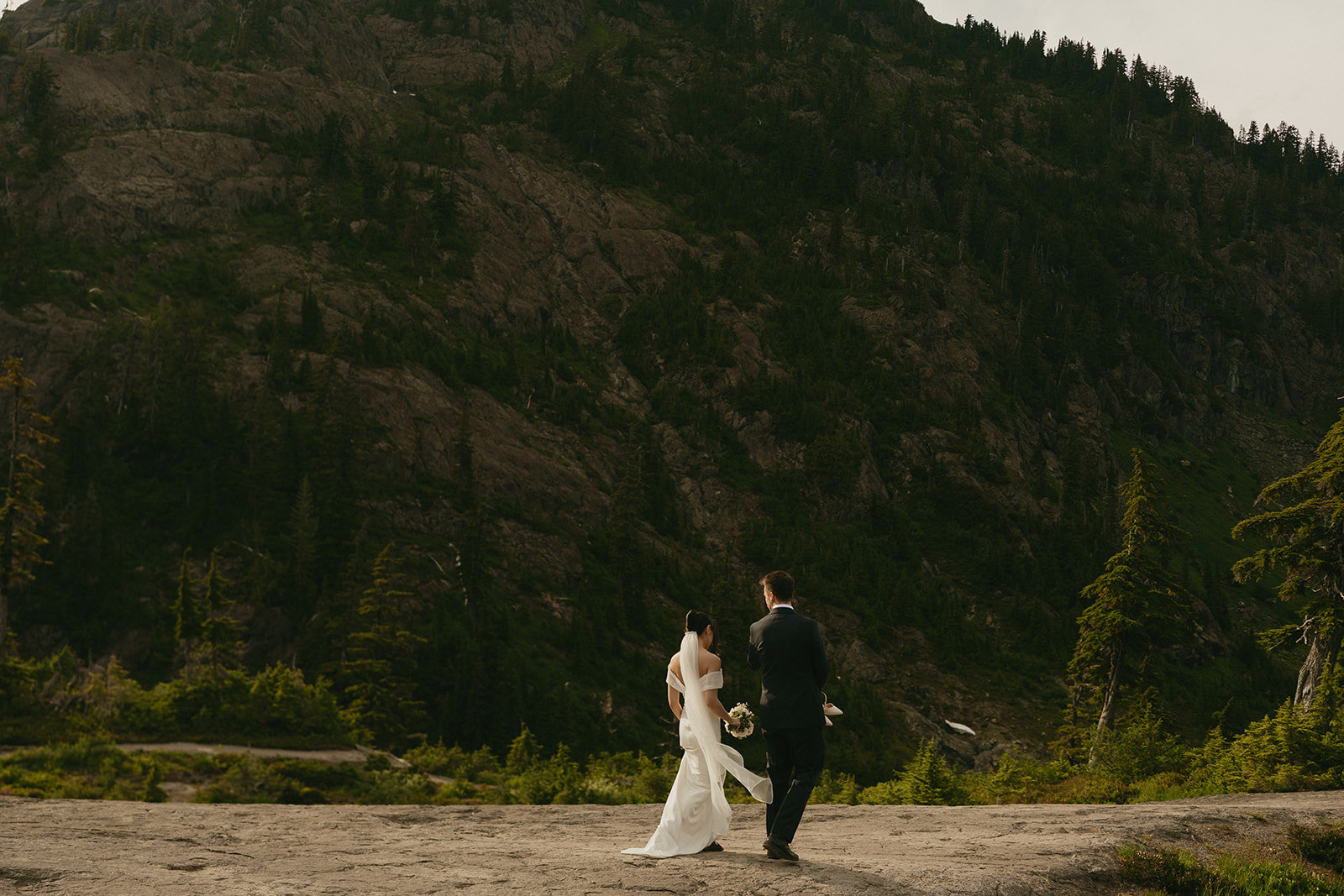 Bride and groom walk together along a rugged trail at their Washington mountain elopement.