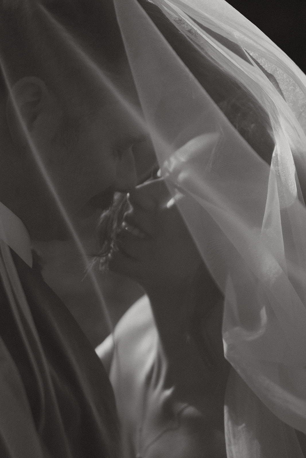 Romantic close-up of a bride and groom kissing under a flowing veil.