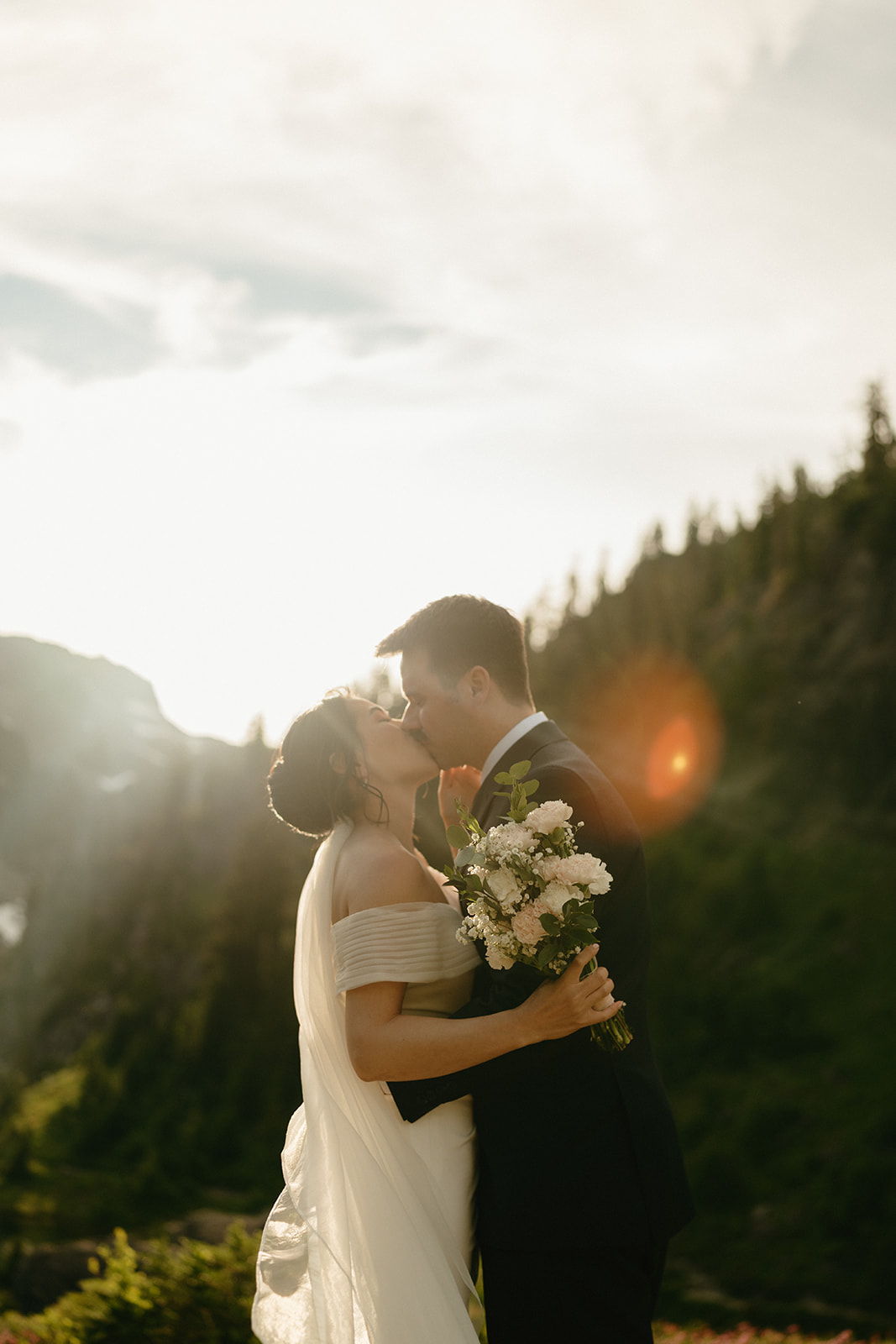 Couple kisses in golden light, bouquet in hand, while eloping in Washington’s backcountry.