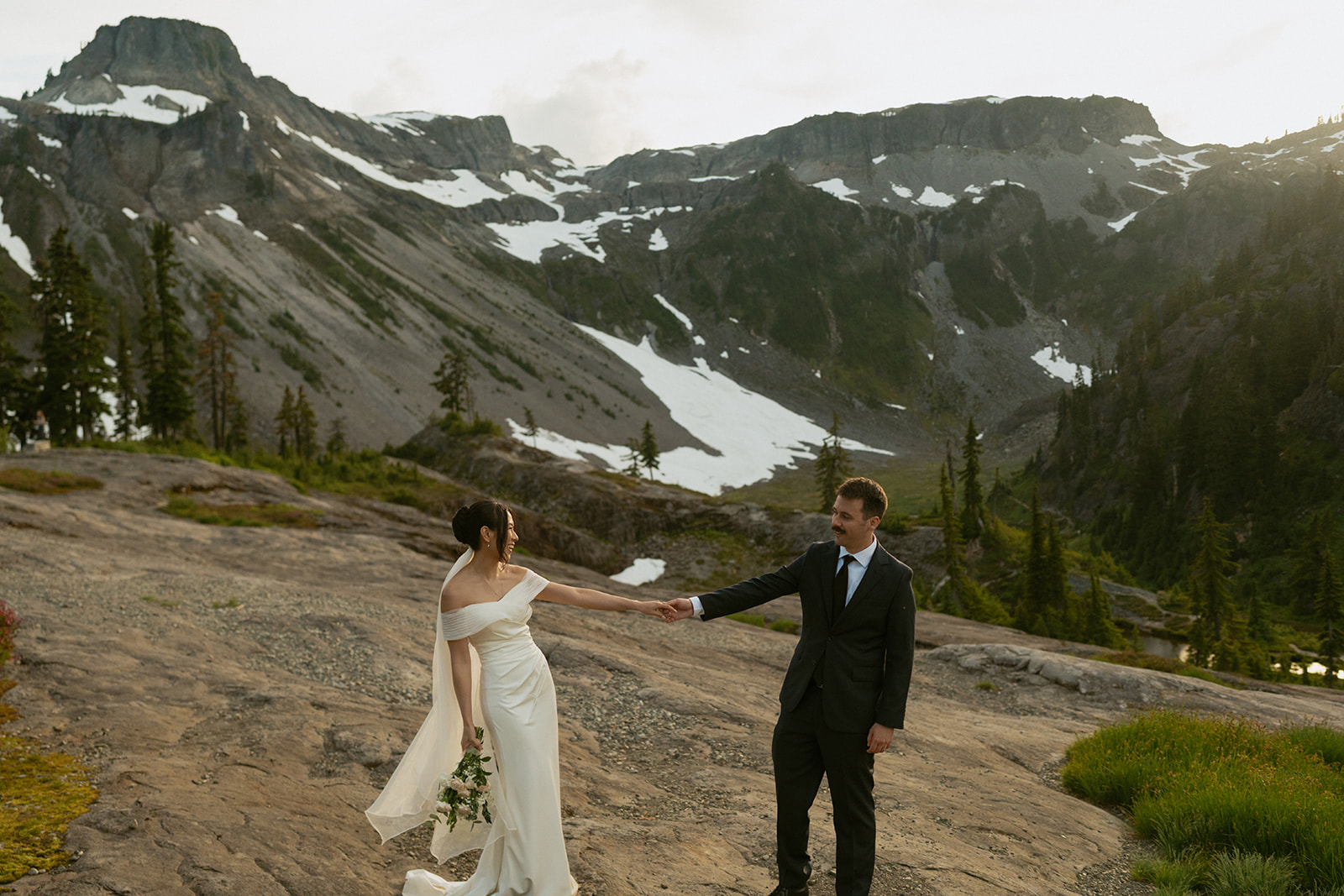 Bride and groom walk hand-in-hand across alpine rock, mid-elopement in Washington.