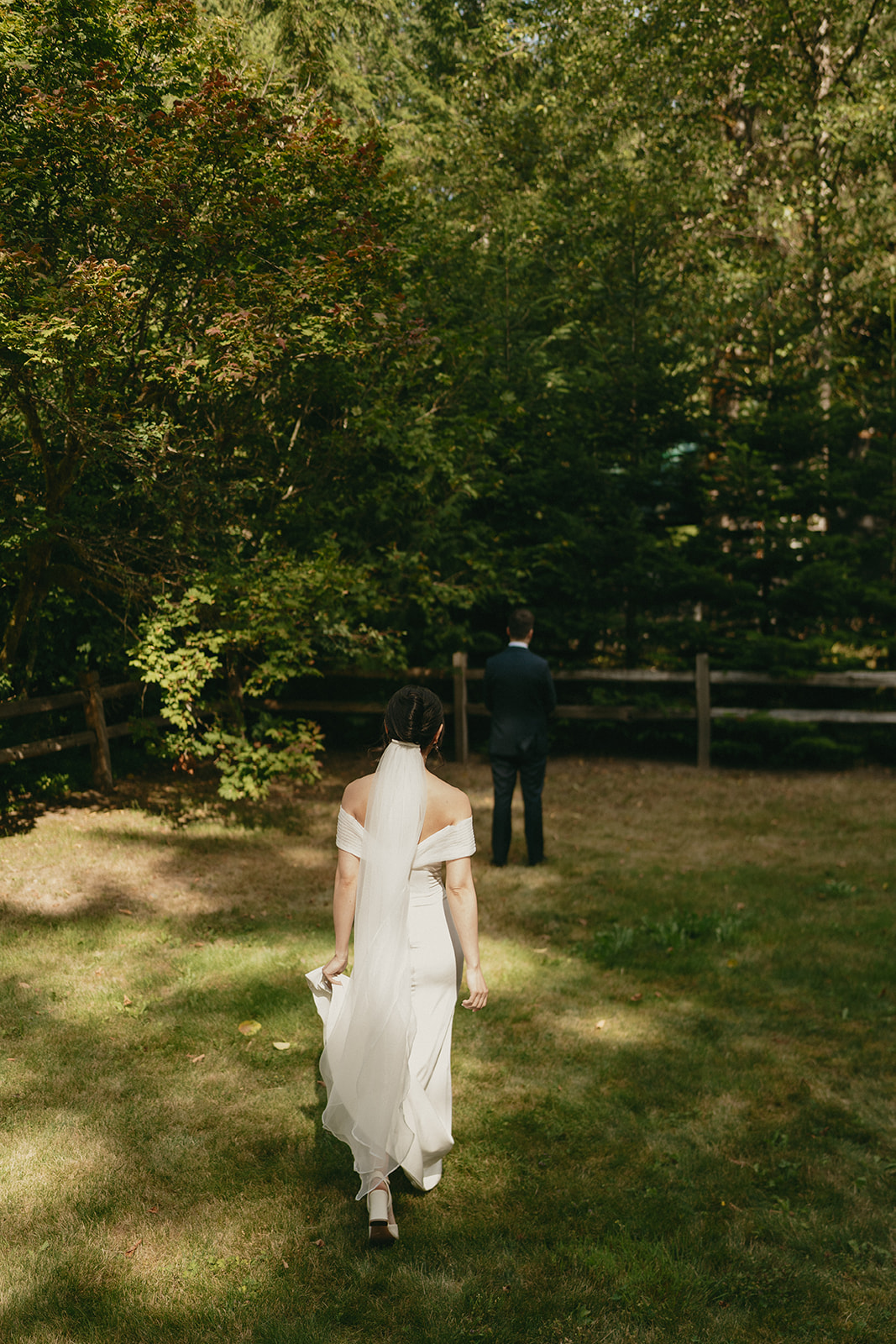 Bride walking barefoot across a sunlit clearing, about to surprise her groom while eloping in Washington.
