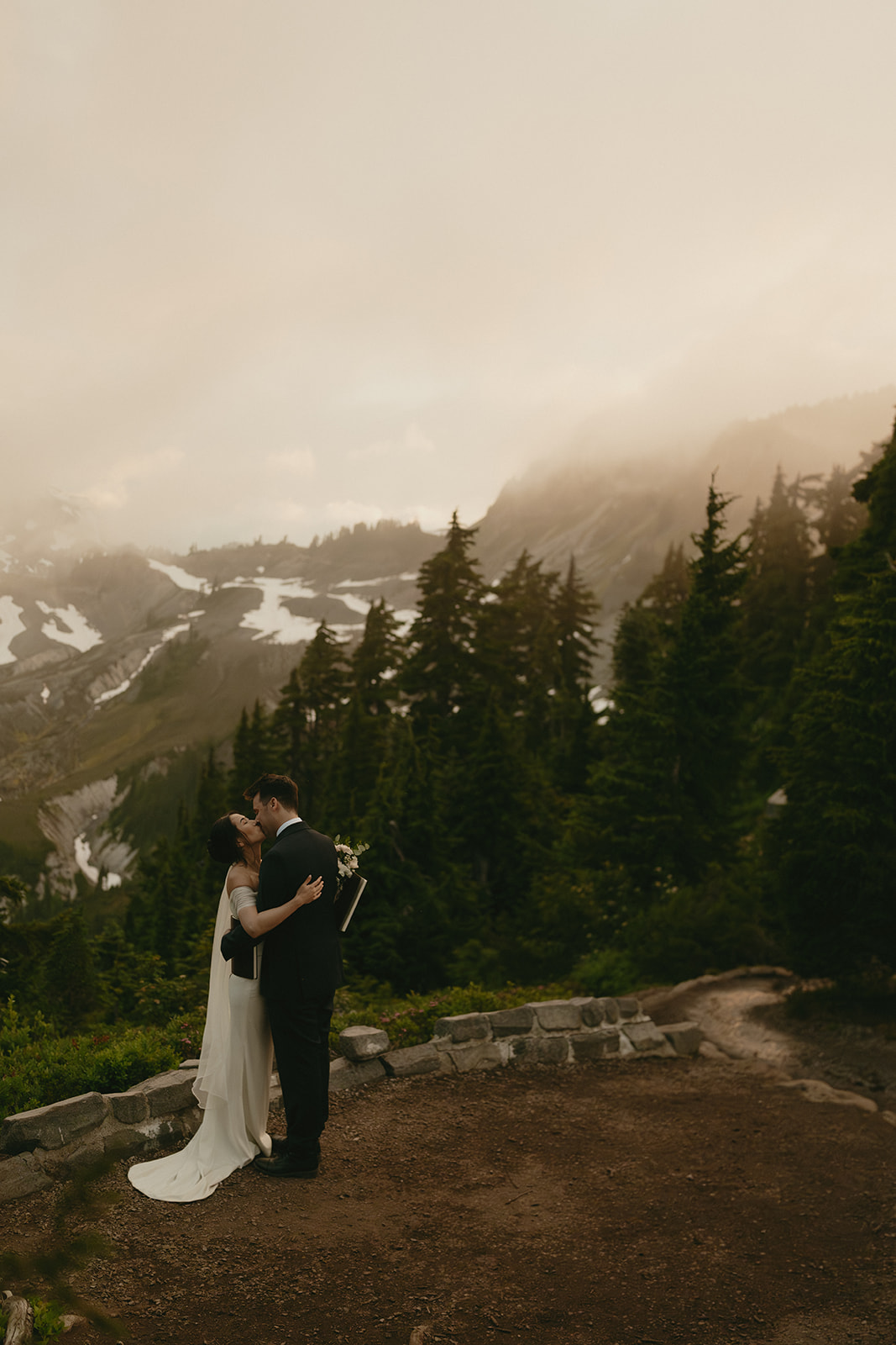 Bride and groom kiss surrounded by mountains and tall trees while eloping in washington